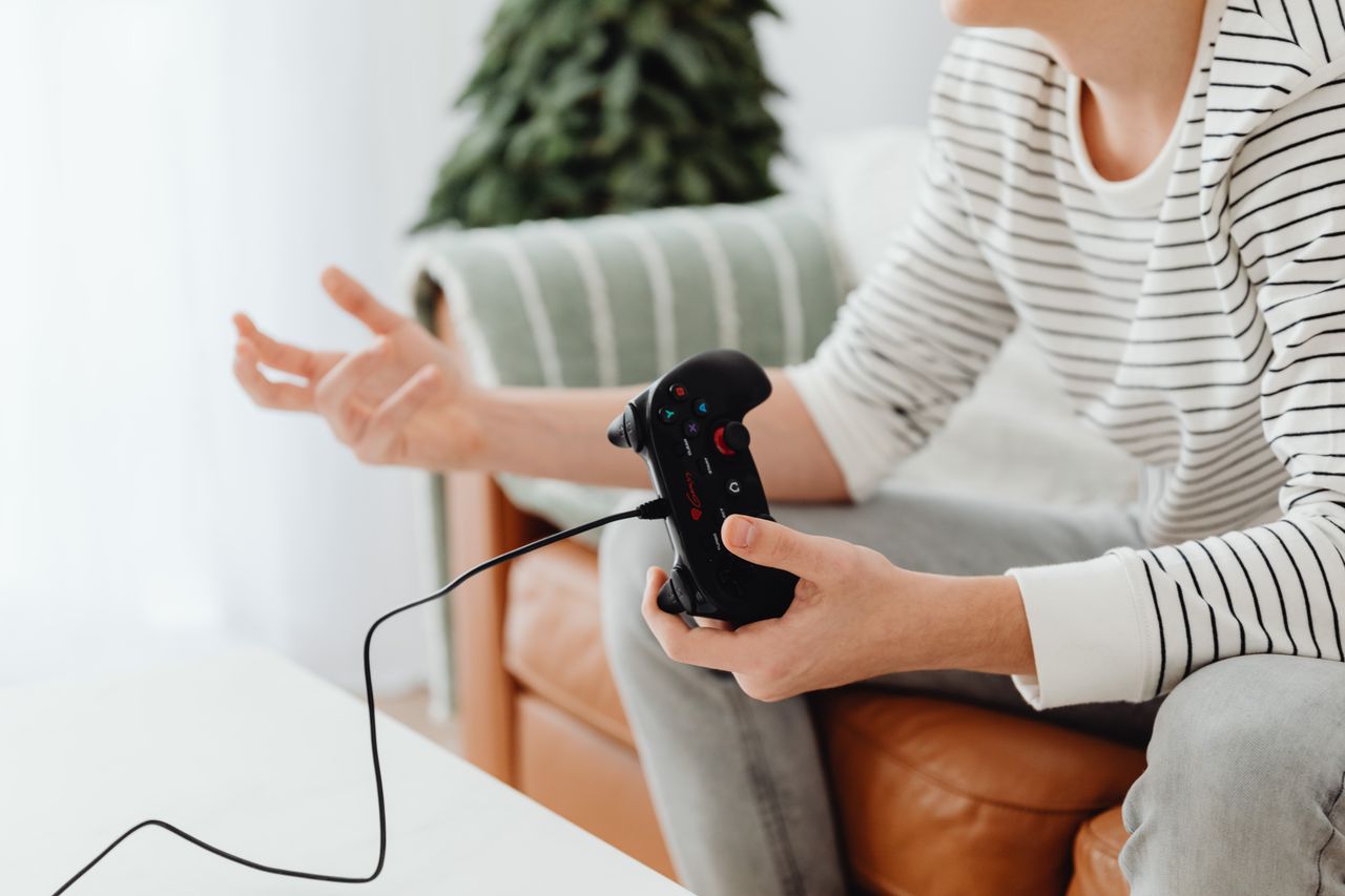 Close-up of a person playing video games at home with a wired controller on a couch.
